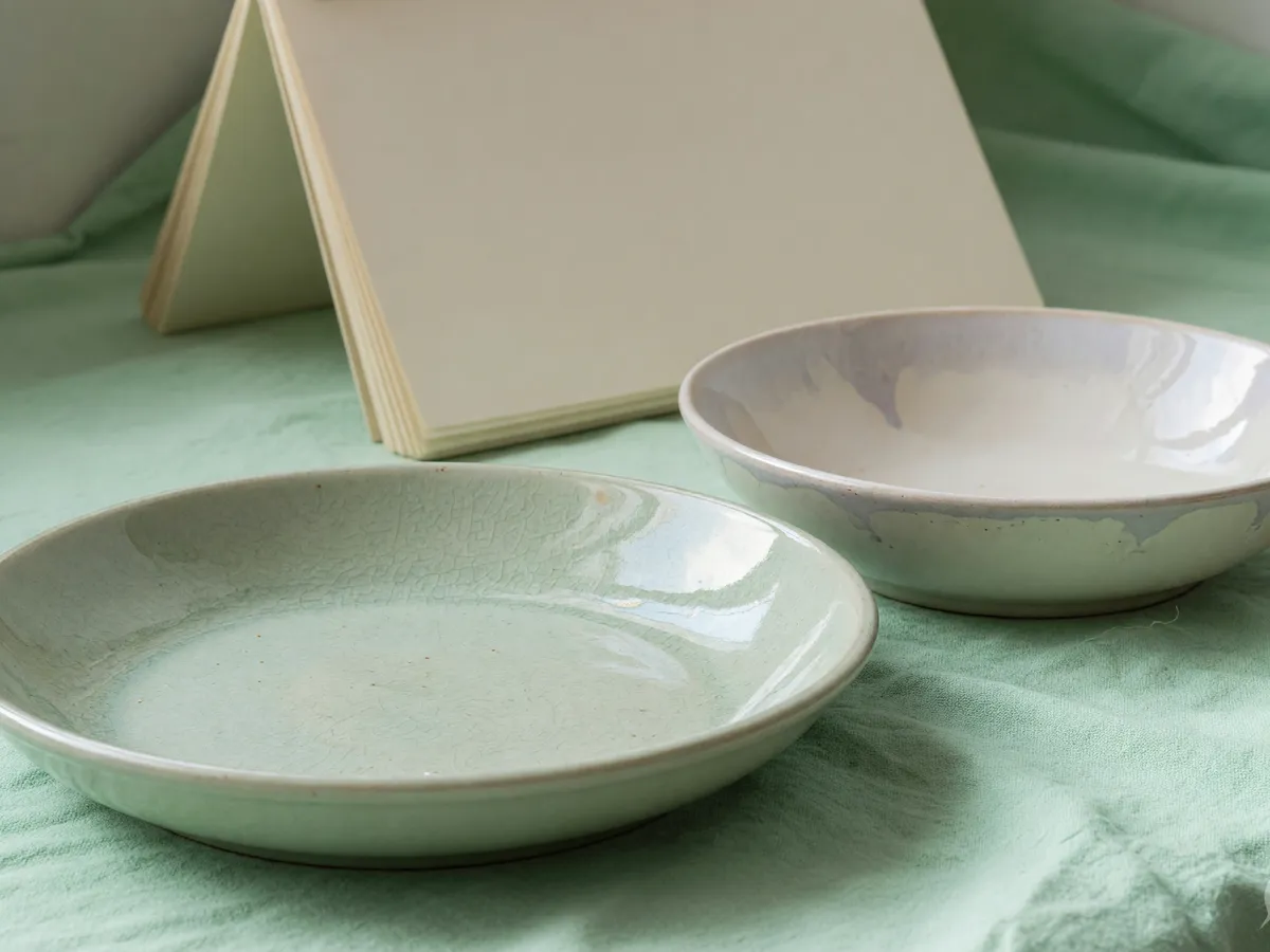 Two empty ceramic dishes on mint cloth with a tented blank folio